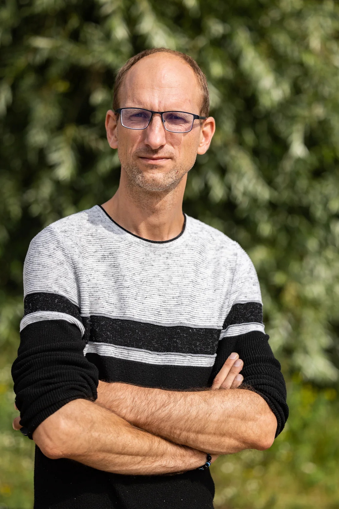 Aigars Kauliņš, photographed outdoors, facing the camera with arms folded